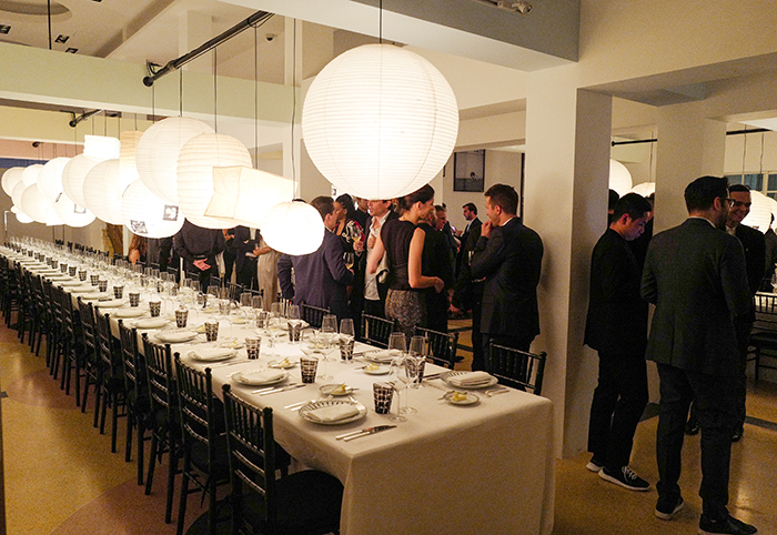 Guests beside a long dinner table beneath glowing lanterns at the Dior Homme Black Carpet celebration at The Webster.