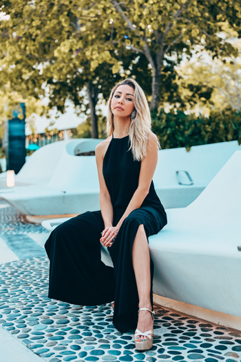 Karen Huggins wearing a black Osklen jumpsuit while seated outdoors