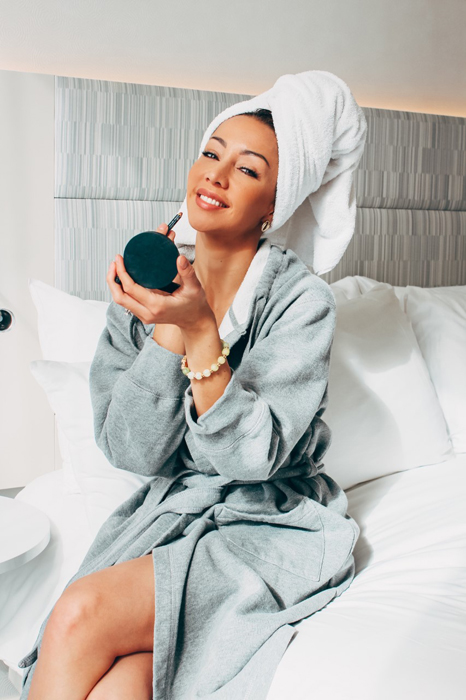 Karen Huggins in a bathrobe and towel seated on a hotel bed