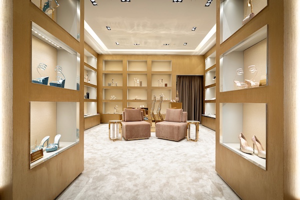 Illuminated footwear displays lining a gold-toned corridor with two pink velvet chairs.