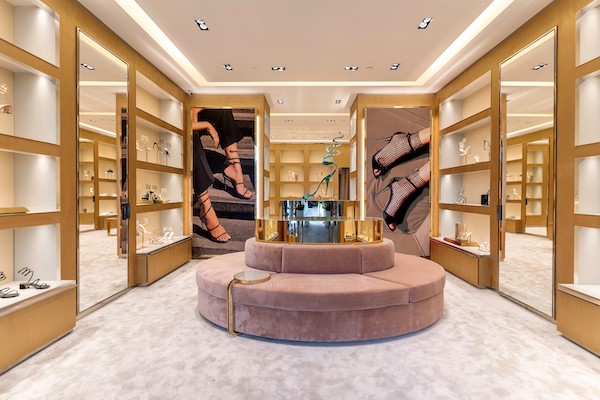 Oval pink velvet sofa surrounded by illuminated shoe shelves and gold walls.