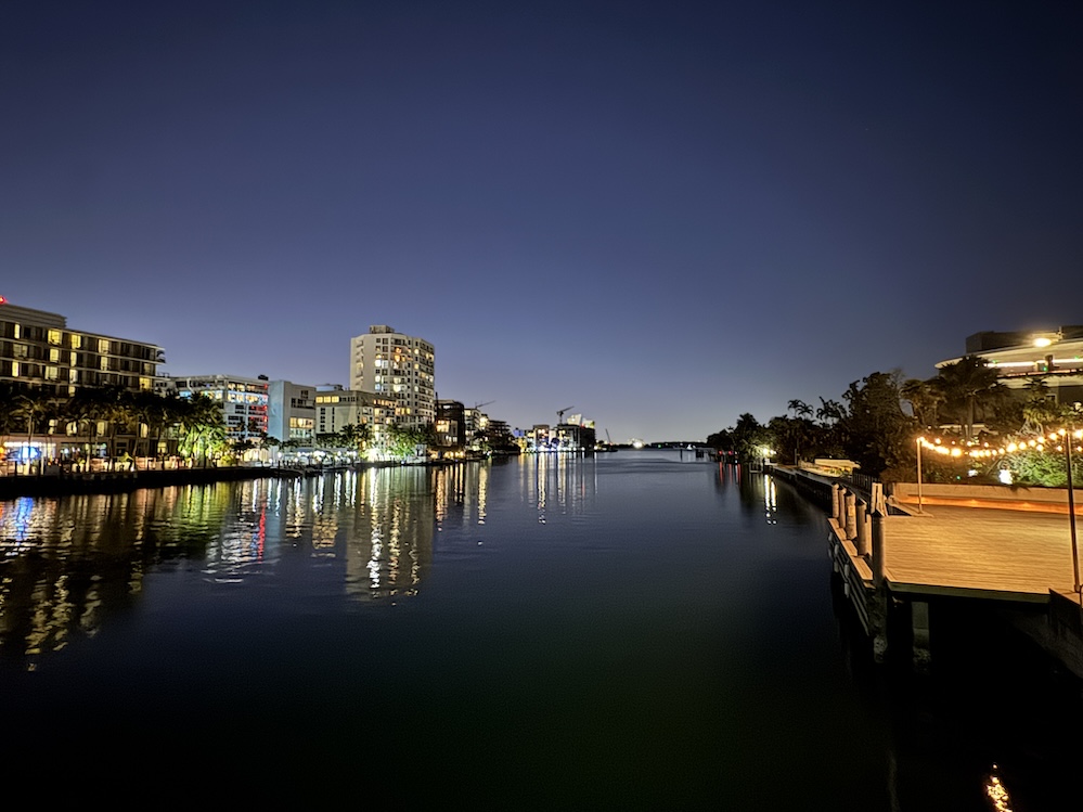 Waterfront buildings and lights reflected on calm water in Bay Harbor at dusk