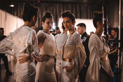 Models gathered backstage wearing coordinated light-colored outfits.